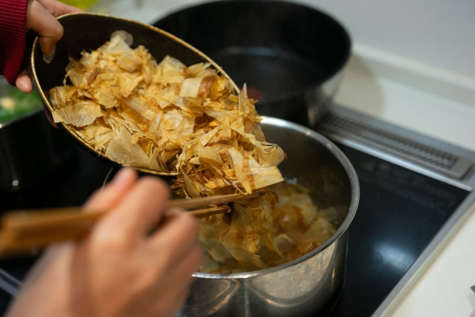 Katsuobushi wordt met eetstokjes in een pan met bouillon gedaan
