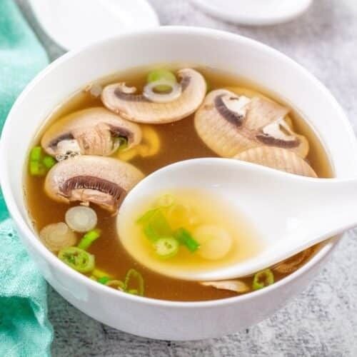 Kom heldere bouillon met champignons, lente-ui en een witte lepel