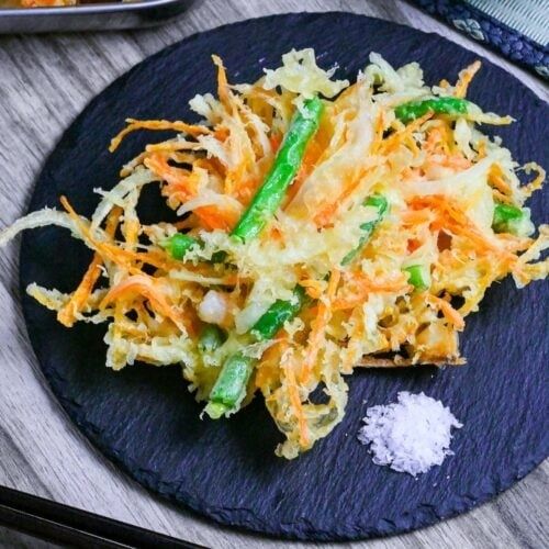 Goudbruine groentetempura met wortel en sperzieboon op een zwarte schaal
